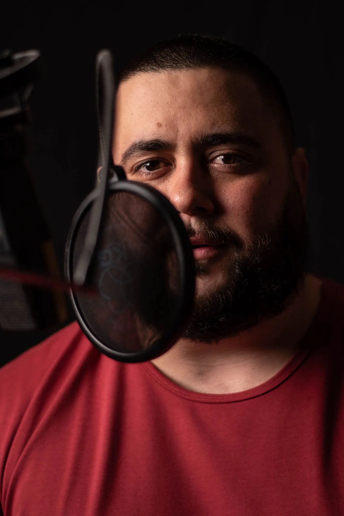MC Solar Wind in the vocal booth, red tee, behind a pop filter
